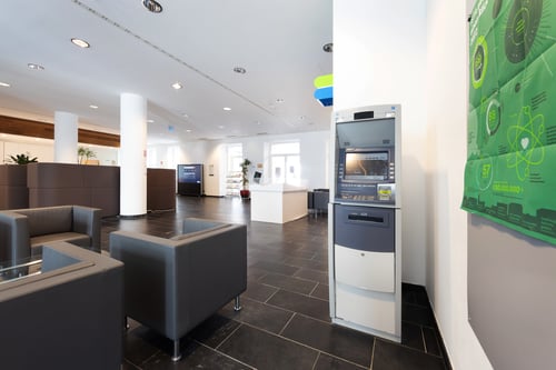 Schrägansicht des Bankomaten aus mittlerer Entfernung, die den gesamten Automaten und den umgebenden Bereich zeigt.