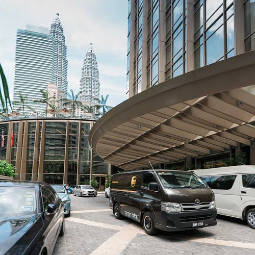 a brown UPS van outside the lobby roundabout of a skyscraper