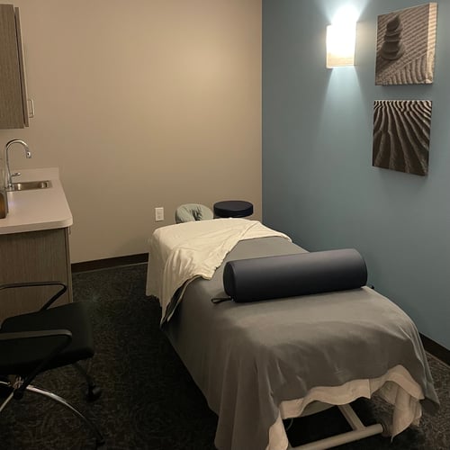 Private massage therapy room featuring a comfortable table, calming blue accent wall, and zen artwork.