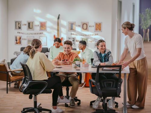 Fusion Academy students working on homework at a table, and students playing games together in the background.