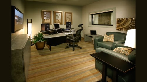 Professional audio editing suite with a large desk, studio monitors, ergonomic chair, and green leather sofas.