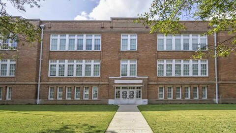 Exterior view of a historic red brick building with large white-trimmed windows and a central entrance.