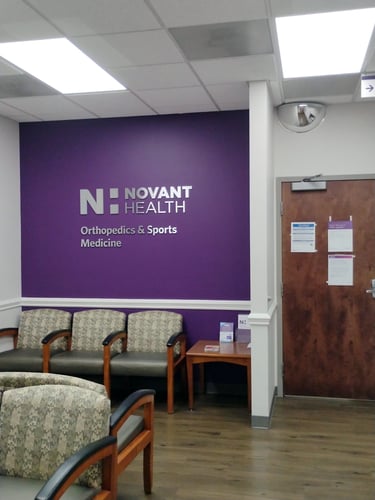 Waiting room with chairs and a purple wall with Novant Health signage.