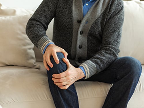 man sitting on couch experiencing knee pain