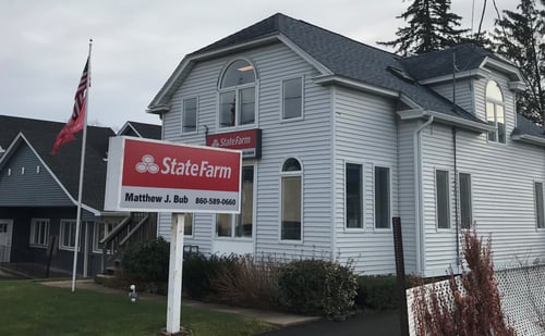 White building with red and white State Farm sign hanging on building with two flags