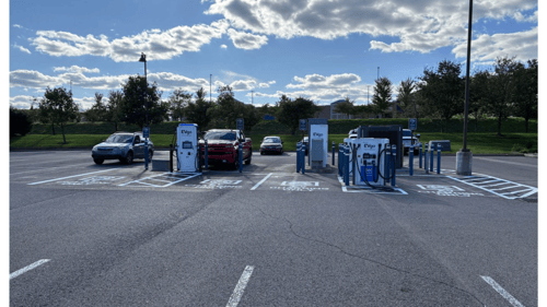 Several EVgo fast charging units installed in marked parking spaces at a public charging station, with EVgo logos on the chargers, protective bollards around each unit. CCS chargers featured in the image.