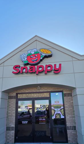 Exterior of the Snappy Pizza Florence location with red tomato logo signage above the entrance and glass doors below.