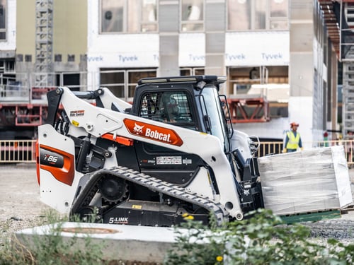 Operator is moving a pallet of cinder blocks with a Bobcat T86 compact track loader with pallet fork attachment.