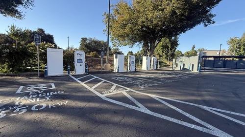 Several EVgo fast charging units installed in marked parking spaces at a public charging station, with EVgo logos on the chargers, protective bollards around each unit