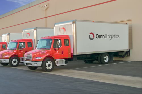 Three red and white delivery trucks with Omni Logistics logos being loaded at freight forwarding distribution center dock doors