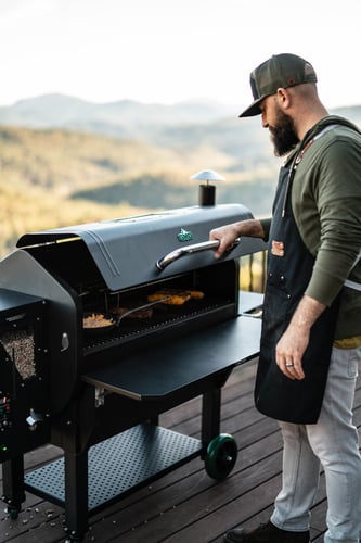 Asheville Peak pellet grill with man opening lid, installed on mountain patio overlooking landscape valley