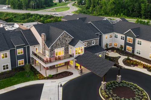 Birdeye view of the entrance of a senior living community with stone, siding, and a circular driveway