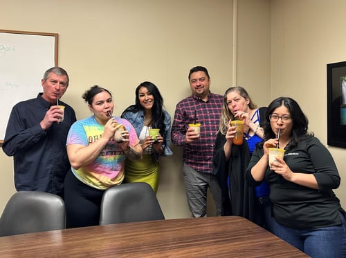 6 people standing behind a conference table sipping on bubble tea.