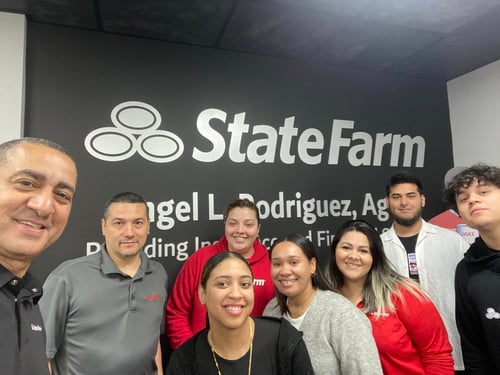 Agent Angel Rodriguez standing and smiling with seven team members inside of agency