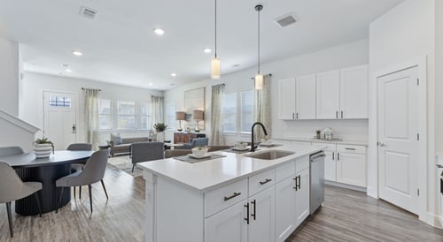 Spacious open-concept kitchen and living room with white cabinets, modern lighting, and natural light.