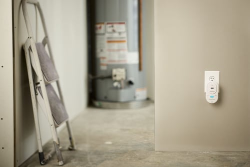 An image of a CO detector plugged into the wall, a step-stool and a water heater is in the background.