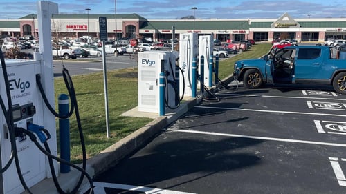 Several EVgo fast charging units installed in marked parking spaces at a public charging station, with EVgo logos on the chargers, protective bollards around each unit.