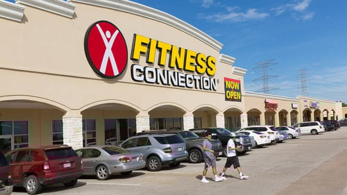 Two men walking in front of car lined X Fitness Connection