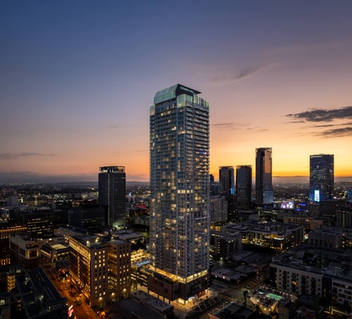 A cityscape at dusk with a tall building in the foreground at Olympic + Hill in Los Angeles, CA