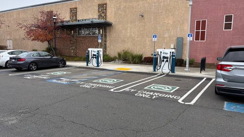 Several EVgo fast-charging units installed in marked parking spaces at a public charging station, with EVgo logos on the chargers, protective bollards around each unit
