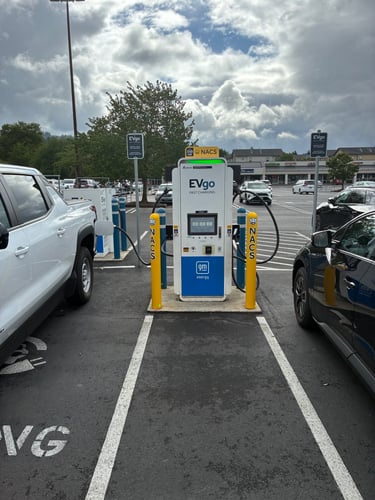 NACS EVgo fast charging unit installed in marked parking space at a public charging station, with EVgo logos on the charger,  and yellow protective bollards around the unit