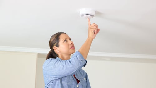 A woman tests her smoke alarm by pushing the test button.