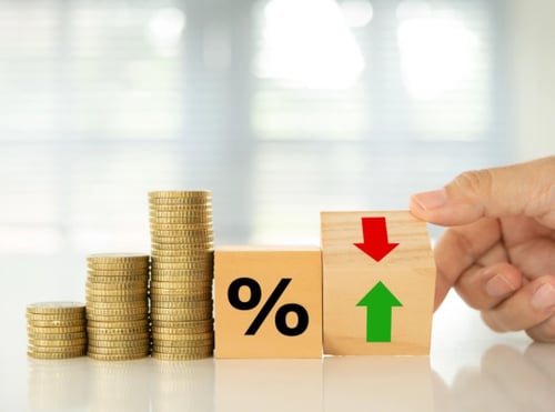 Hand holding wooden block with green upward arrow next to stacked coins and percentage symbol with red downward arrow.