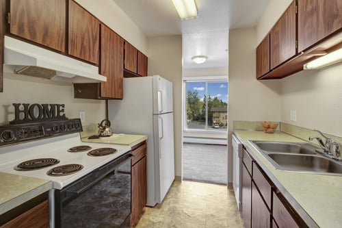 Compact kitchen with warm wood cabinets at Castle Apartment Homes in Anchorage, AK 99503