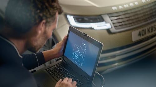 Technician using a laptop to run diagnostics in front of a Range Rover with headlights on.