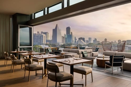 Modern restaurant dining area with minimal furniture and clear floor-to-ceiling windows showing the city of Atlanta.