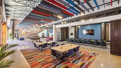 Open coworking area with colorful ceiling panels, shared desks, and a welcoming atmosphere.