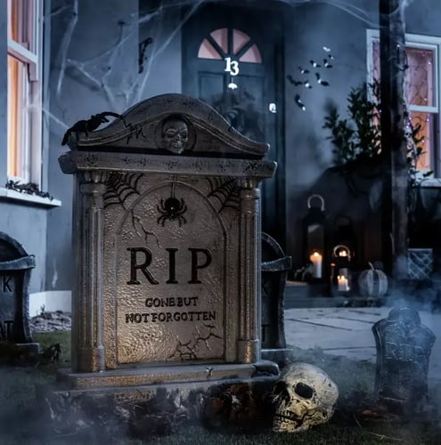 Halloween gravestone decoration in a front garden with cobwebs, skull props and lantern lights