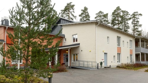 Peuramäen kaksikerroksinen rakennus kuvattuna siten, että etualalla näkyy liuska sisäänkäyntiin.