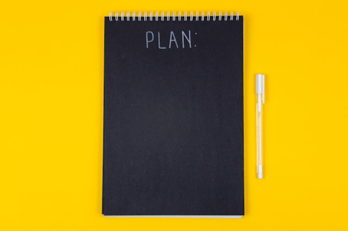 A black notebook and white pen laid against a yellow background.