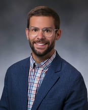 Dr. Edwall Joel smiling in front of a gray background.
