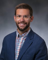 Dr. Edwall Joel smiling in front of a gray background.