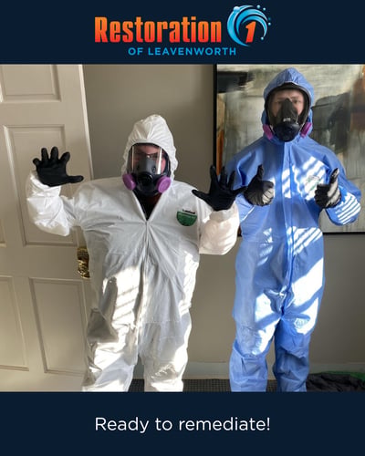 Two Restoration 1 of Leavenworth technicians in protective hazmat suits and respirators pose cheerfully indoors. Caption reads: 'Ready to remediate!