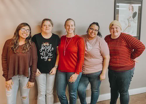 Five people smiling together in front of a grey wall.