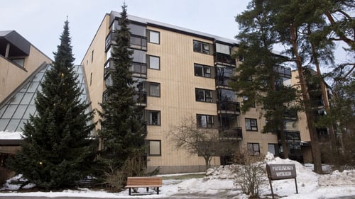 Ulkokuva Kotikalliosta. Rakennus on keltatiilinen. Pihapiirissä on havupuita ja maassa on lunta.