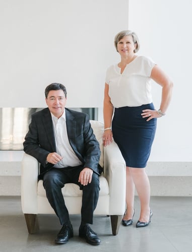 Andrew sitting in a white contemporary chair and Michelle standing in front of a gas fireplace at the Beaverbrook Art Gallery.