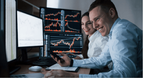 two people smiling while reviewing multiple screens of charts