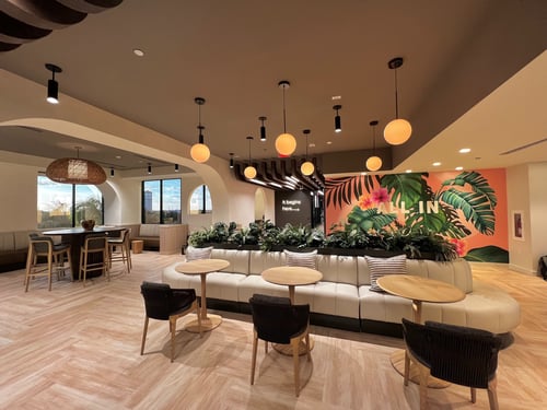 Break room area with a high-top table and chairs and low top table with chairs on one side and bench seating on the other.