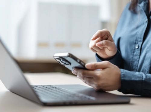 Person using a laptop and a phone on a desk.
