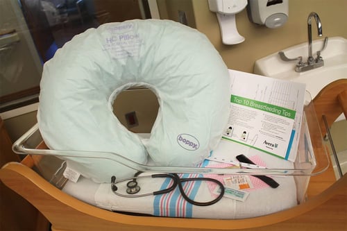 A boppy pillow, stethoscope and card with breastfeeding tips in a bassinet