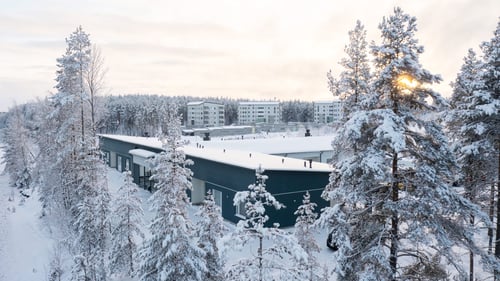 Luminen maisema, jossa näkyy puiden latvojen takana turkoosin värinen rakennus, jossa toimii Rinnekodit Tähtisumun yksikkö.