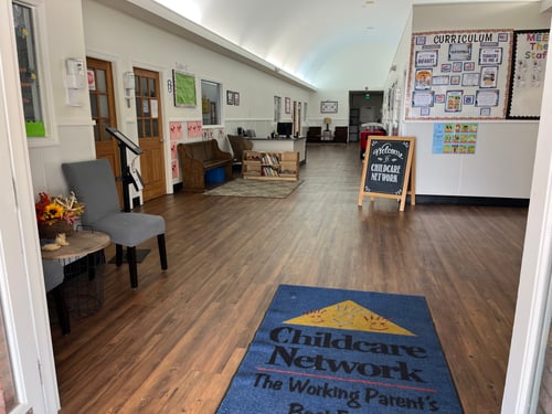 Bright and welcoming lobby with chairs for parents and a colorful bulletin board displaying cute moments from the daycare.