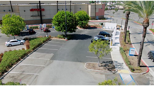 aerial image of a 16 stall evgo charging station. Multiple EVgo fast charging units installed in marked parking spaces at a public charging station, with EVgo logos on the chargers, protective bollards around each unit. NACS and CCS chargers featured in the image.