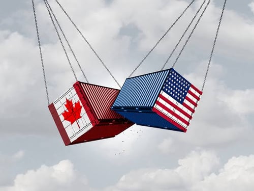 A Canadian flag and American flag, each painted on shipping containers, swing toward each other against a cloudy sky—symbolizing the tense trade relationship and economic interdependence between Canada and the United States