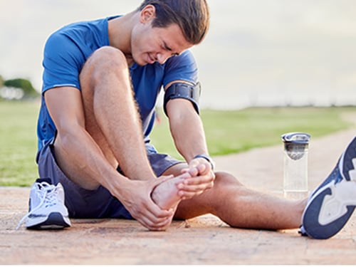 athletic man outdoors massaging feet from foot pain