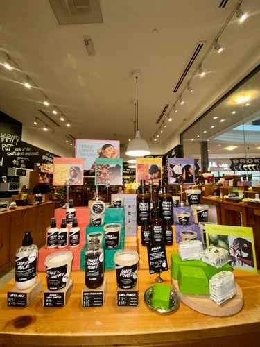 Display of different packaged and unpackaged haircare products. Some stood on coloured plinths. The rest of the shop is visible in the background.